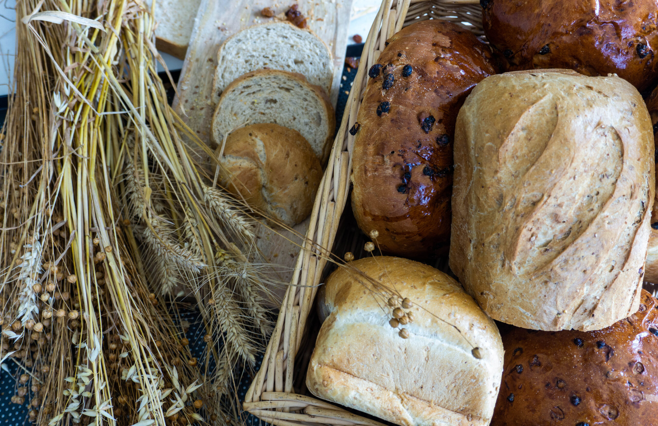 Een broodmand met diverse broden, gelegen naast graan en gesneden brood.